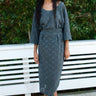 Woman wearing a gray lace tee and skirt standing in front of a white bench with green foliage in the background.