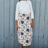 Woman wearing a floral skirt and white blouse against a wooden fence.