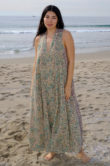 A woman at the beach wearing a sleeveless maxi caftan in a beige ground tapestry, turquoise flower handloom.