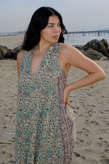 A woman at the beach wearing a sleeveless maxi caftan in a beige ground tapestry, turquoise flower handloom.