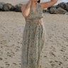 A woman at the beach wearing a sleeveless maxi caftan in a beige ground tapestry, turquoise flower handloom, featuring a matching obi belt.