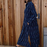 A woman standing in front of a wooden gate wearing black ikat shirt dress with long sleeves.