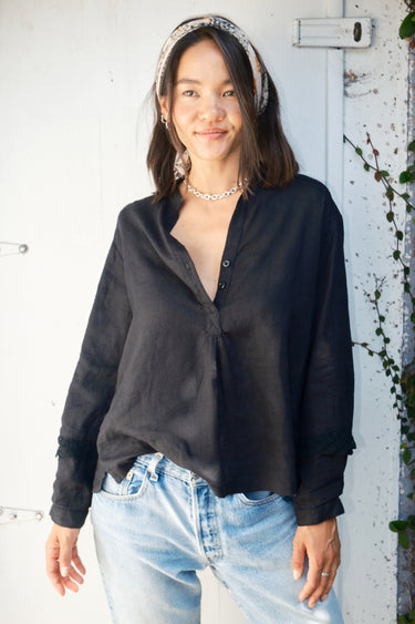 A woman wearing a black linen blouse with long sleeves and a band collar, paired with jeans.