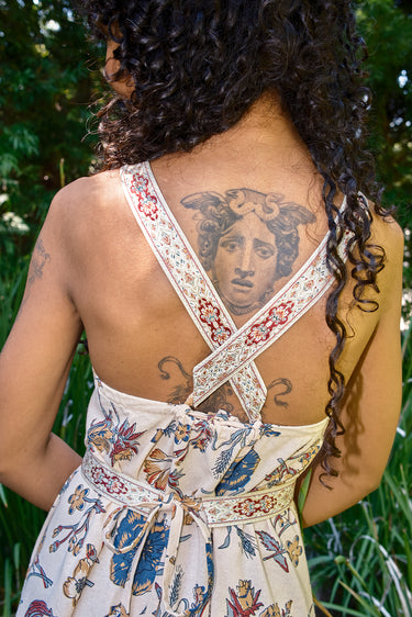 Woman wearing a floral dress with tattoos visible on her back against a natural background