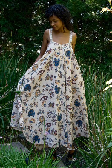 Woman in a floral dress standing in a natural setting with greenery.
