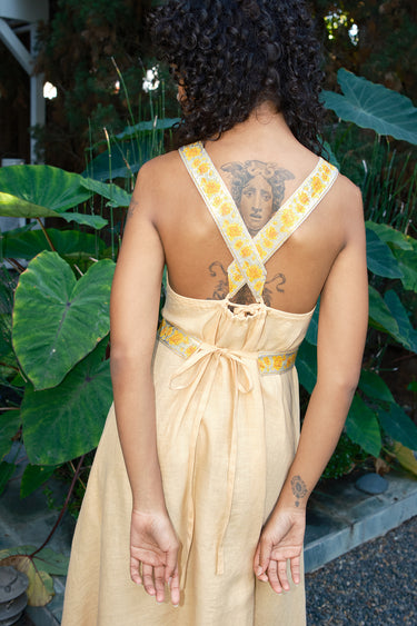 Person wearing a light yellow dress with yellow floral straps in an outdoor setting