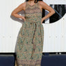 A woman standing by a white fence wearing a beige ground turquoise flower tapestry wrap maxi dress.