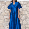 woman standing by stone wall wearing a sapphire blue zip front dress with black boots