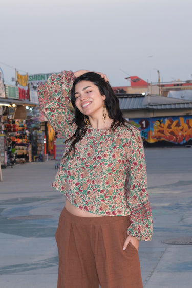 A woman standing on the sidewalk wearing a nutmeg colored Bermuda short, long sleeve top. The background includes graffiti and a building.