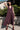 Woman wearing a dark fig  dressstanding outdoors with greenery in the background
