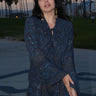 A woman standing at Venice Beach at dusk wearing dark blue midnight sky handloom tapestry shirt with bell sleeves.