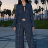 A woman standing at Venice Beach at dusk wearing dark blue midnight sky handloom tapestry low rise trouser and a matching shirt with bell sleeves.