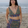 A woman standing on the beach wearing a multicolored floral tapestry bra top and a matching skirt.