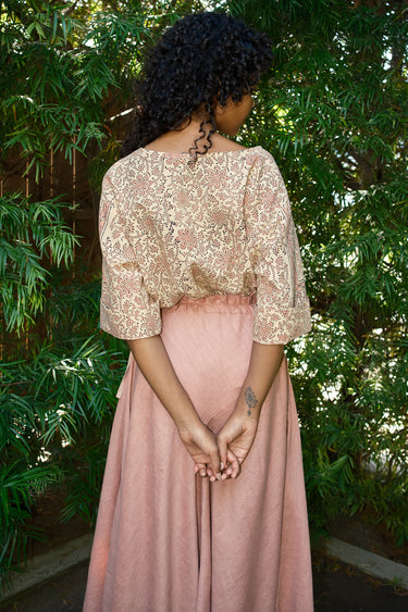 Person wearing a floral top and pink skirt standing in front of green foliage