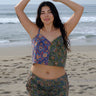 A woman standing at the beach wearing a floral tapestry camisole cut using both green and blue tapestry of the same print tapestry mixed together. Worn with matching pants.