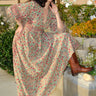 A woman standing outside wearing a beige ground with red and brown belted floral caftan.
