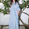 A woman standing outdoors wearing a blue and white patterned maxi dress with three quarter balloon sleeves and cell phone pockets.