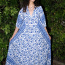 A woman standing in a garden wearing a blue and white floral maxi dress with three quarter balloon sleeves and a V-neck.