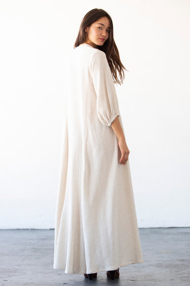 woman standing in photo studio wearing a maxi alabaster caftan with deep v neck and balloon sleeves, back view