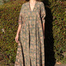 A woman wearing a maxi caftan with a floral pattern in a color that could be described as celadon green ground with tan, brown and blue, standing outdoors.