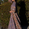A person wearing a traditional blue caftan with a paisley pattern and a belt, standing outdoors.