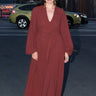 A woman standing outside in the street wearing a raisin osnaburg maxi caftan with long full sleeves and a belt.