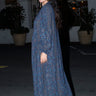 A woman standing outside a night wearing a long sleeve maxi caftan and sandals. The caftan is cut in  midnight sky handloom tapestry, side view.
