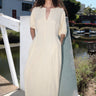 A woman standing outside by a canal wearing an alabaster off white maxi dress with shape from princess panels.
