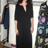 A woman standing inside wearing a black maxi dress with shape from princess panels.