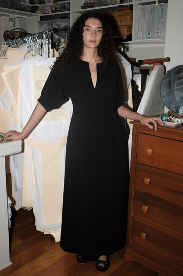 A woman standing inside wearing a black maxi dress with shape from princess panels.