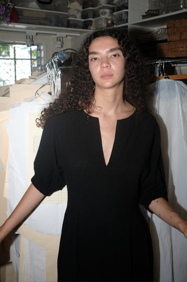A woman standing inside wearing a black maxi dress with shape from princess panels.