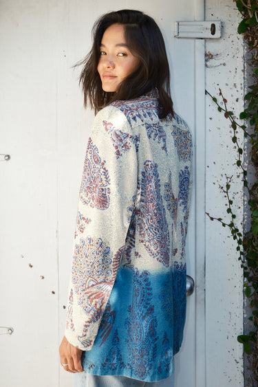A woman wearing a double-breasted jacket with an indigo and blue pattern, and jeans. The jacket is dipped in indigo dye and has pockets on the inside.
