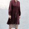 Woman wearing a black fig coat over print skirt with a white background