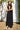Woman wearing a black sleeveless dress standing outdoors against a white wall.