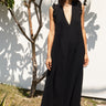 Woman wearing a black sleeveless dress - caftan standing outdoors against a white wall.