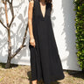 Woman wearing a black sleeveless dress - caftan standing outdoors against a white wall.