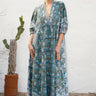Woman wearing a long, patterned caftan standing against a white wall with a cactus plant.