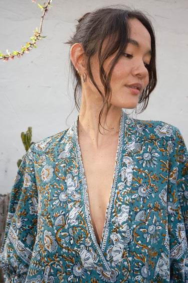 Woman wearing a floral patterned garment against a white wall.
