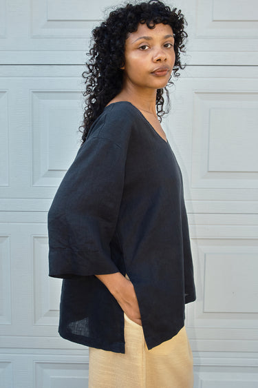 Woman wearing a black top and yellow skirt  against a light gray wall.
