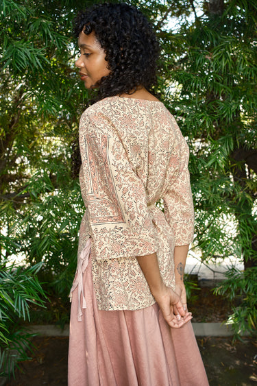 Woman wearing a patterned top and pink skirt in a natural setting
