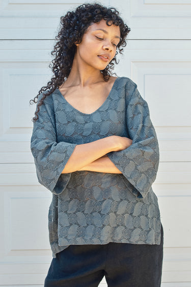 Woman wearing a tpewter gray lace tee against a light background
