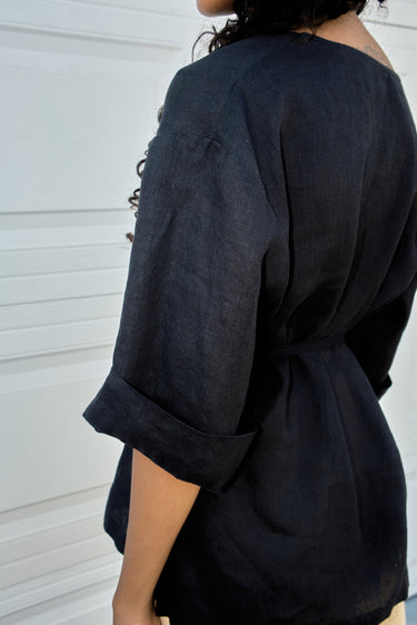 Person wearing a black linen shirt with rolled-up sleeves against a white background