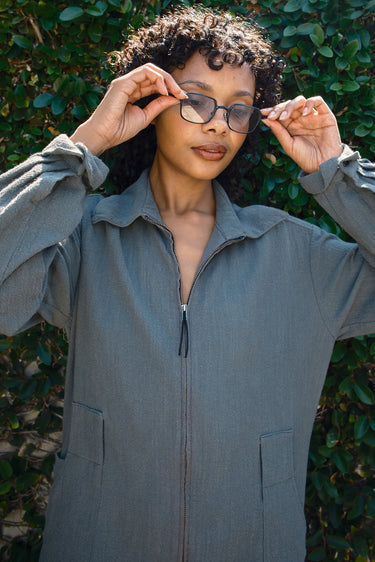 Woman wearing a gray jumpsuit with a blurred green leafy background