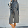 Person wearing a gray bermuda jumpsuit with a belt, standing against a white wall.
