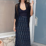 A woman standing in front of a door, wearing a long, black ikat skirt with a geometric tree pattern and a black tank top with a zero waste lace shrug.