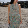 A woman standing at the beach wearing tan with green turquoise flower tapestry draped neck halter top with a matching skirt.