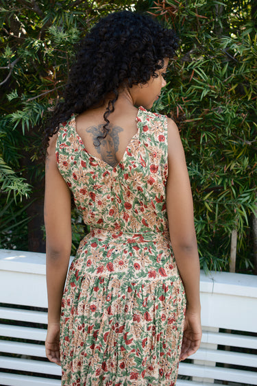Woman wearing a floral dress sitting on a bench with greenery in the background