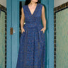 A woman standing on a porch with a blue door wearing a dark blue midnight sky tapestry Maxi Wrap dress, sleeveless.