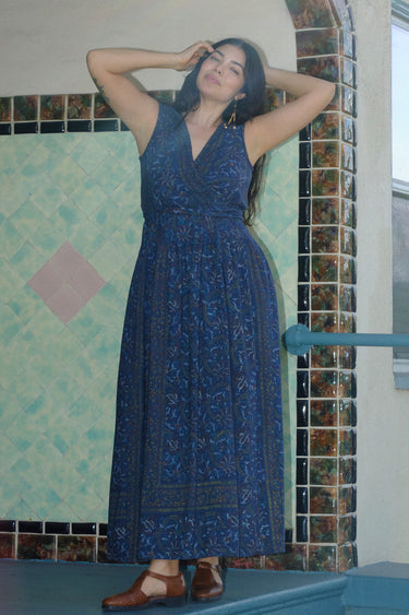 A woman standing on a porch wearing a dark blue midnight sky tapestry Maxi Wrap dress, sleeveless.