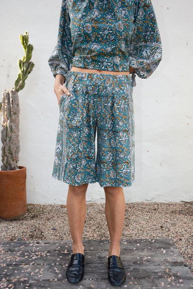 Person wearing a floral outfit standing against a white wall with a cactus plant.